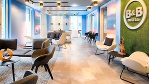 A modern hotel lobby with seating areas, a reception desk, and a B&B logo on the wall. - B&B Hotel Kempten (Kempten)