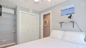 Une chambre à coucher avec un lit, une étagère fixée au mur avec une lampe, un miroir rond et une horloge.
