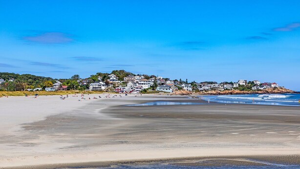 Une plage bordée d’une rangée de maisons, une plage de sable fin et un ciel bleu dégagé.