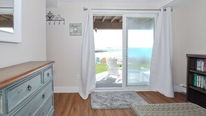 Une pièce comprenant une commode en bois, une bibliothèque, un tapis et une porte-fenêtre coulissante donnant sur un patio aménagé avec du mobilier d’extérieur.