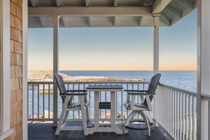 Un espacio al aire libre cubierto con dos sillas y una mesa, con vistas a una costa rocosa y el mar.