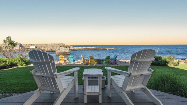 Une terrasse avec deux fauteuils Adirondack blancs, une petite table et des fauteuils Adirondack aux couleurs vives, le tout donnant sur un rivage rocheux et l’océan.