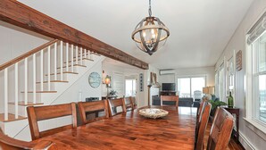 Une salle à manger spacieuse avec une table et des chaises en bois, un lustre et un escalier doté de rampes blanches.
