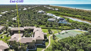 An aerial view of a residential area with multiple buildings, a tennis court, and a beach in the background.