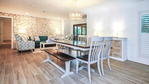 A dining area with a wooden bench, white chairs, and a stone wall.