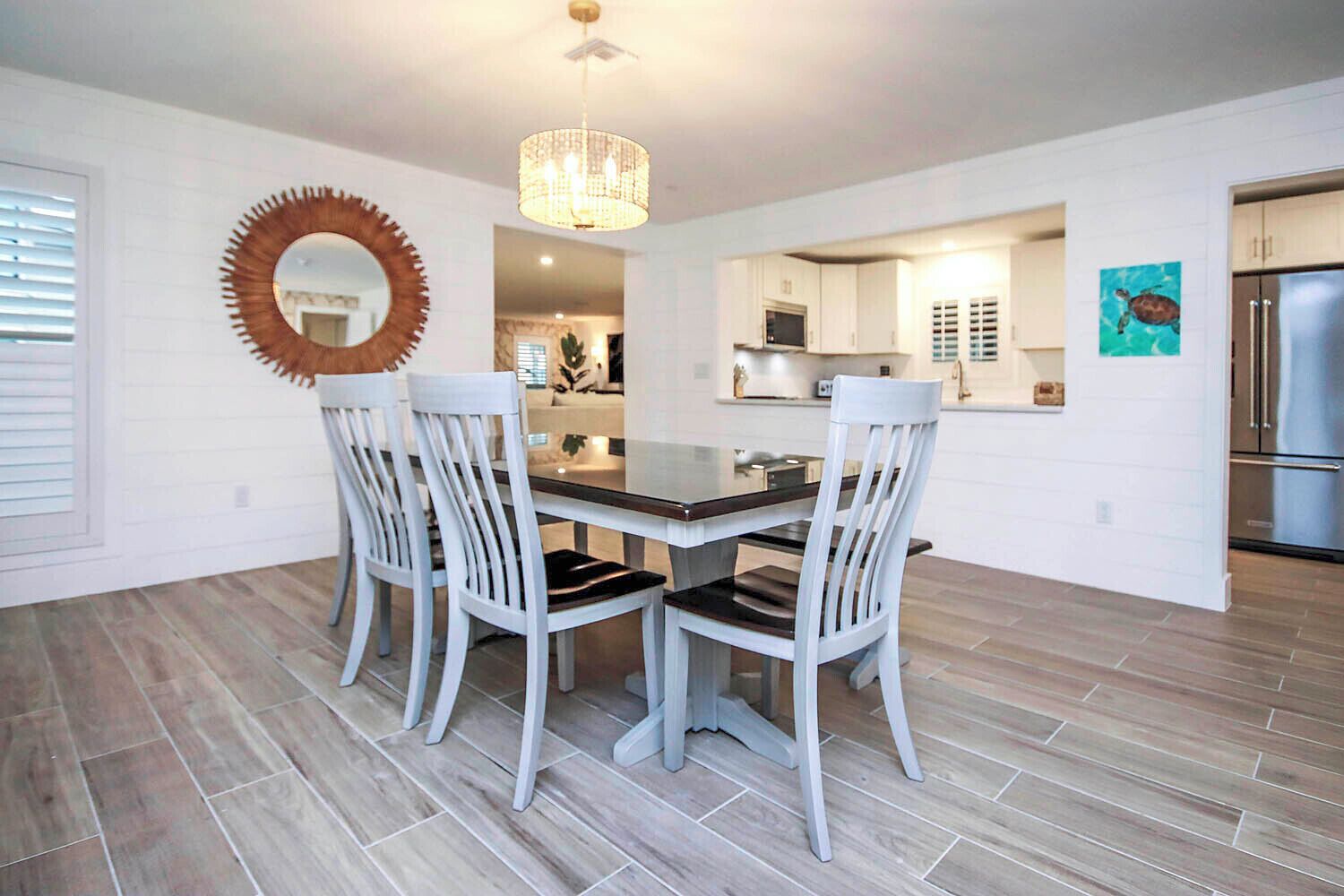 A modern dining area with a round mirror, white chairs, and a chandelier.