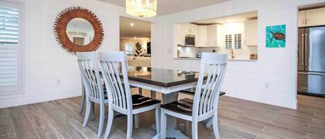 A modern dining area with a round mirror, white chairs, and a chandelier.
