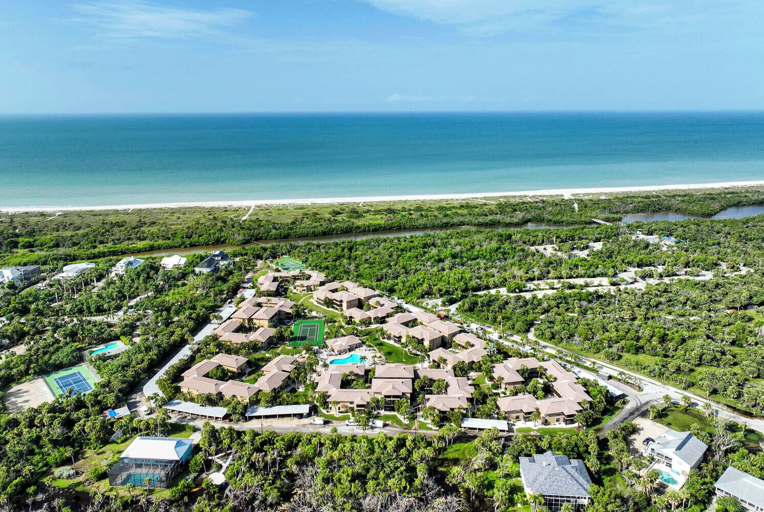 Ovenfra set et resort med flere bygninger, en tennisbane og en strand.