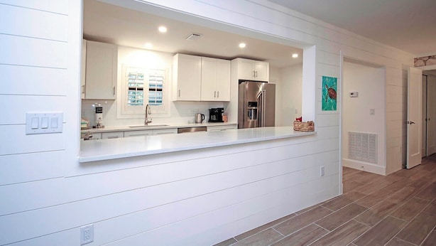 A modern kitchen with white cabinetry, stainless steel appliances, and a large window.