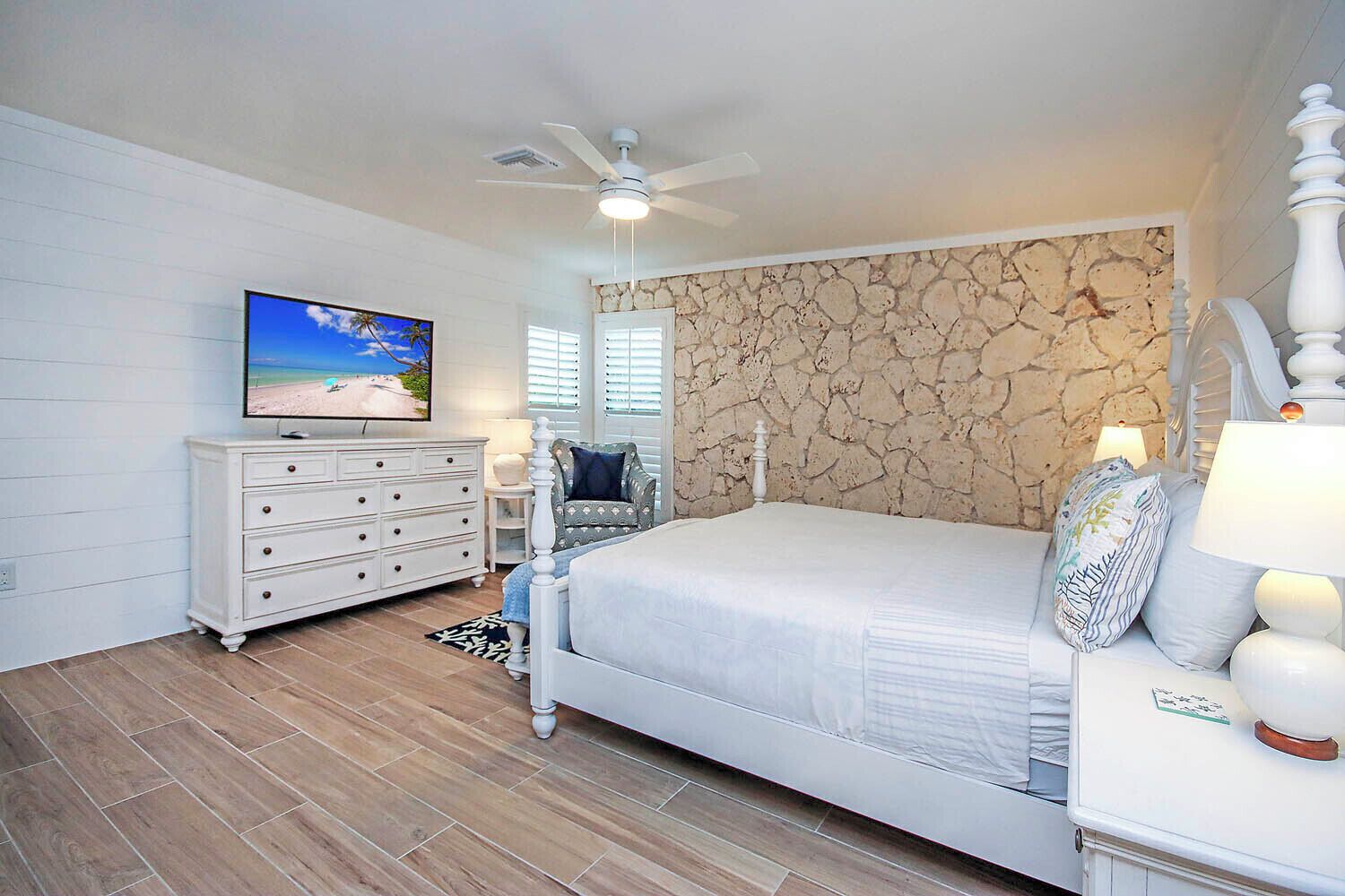 A bedroom with a bed, a dresser, a television, and a ceiling fan.