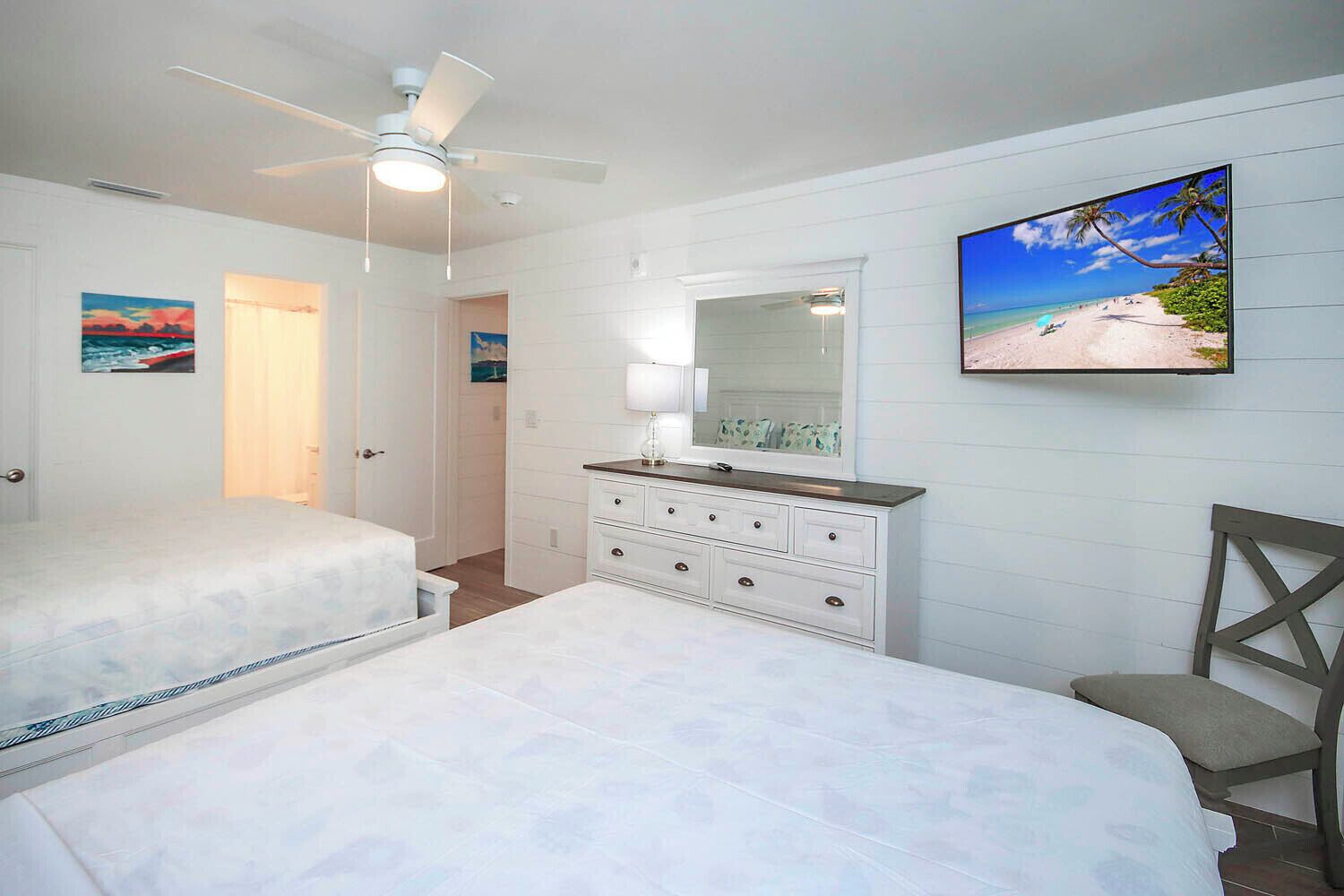 Ein Schlafzimmer mit zwei Betten, einem Schminktisch, einem Deckenventilator und einem Strandbild.
