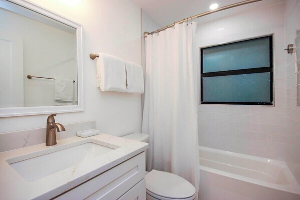 A bathroom with a white sink, a mirror, a toilet, and a bathtub.