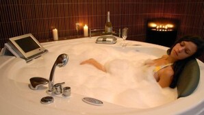 A woman relaxing in a large, modern bathtub with a digital interface, candles, and a bottle of wine, suggesting a luxurious spa setting. - Extreme (Smolyan)