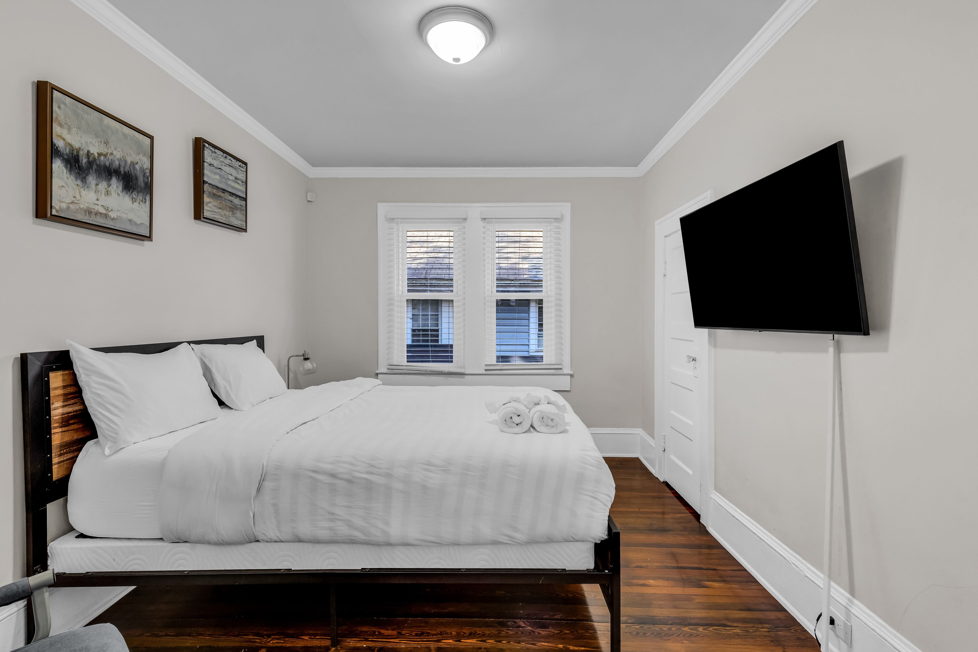 Ein Schlafzimmer mit einem Bett, einem an der Wand befestigten Flachbildfernseher und zwei Fenstern mit Jalousien.