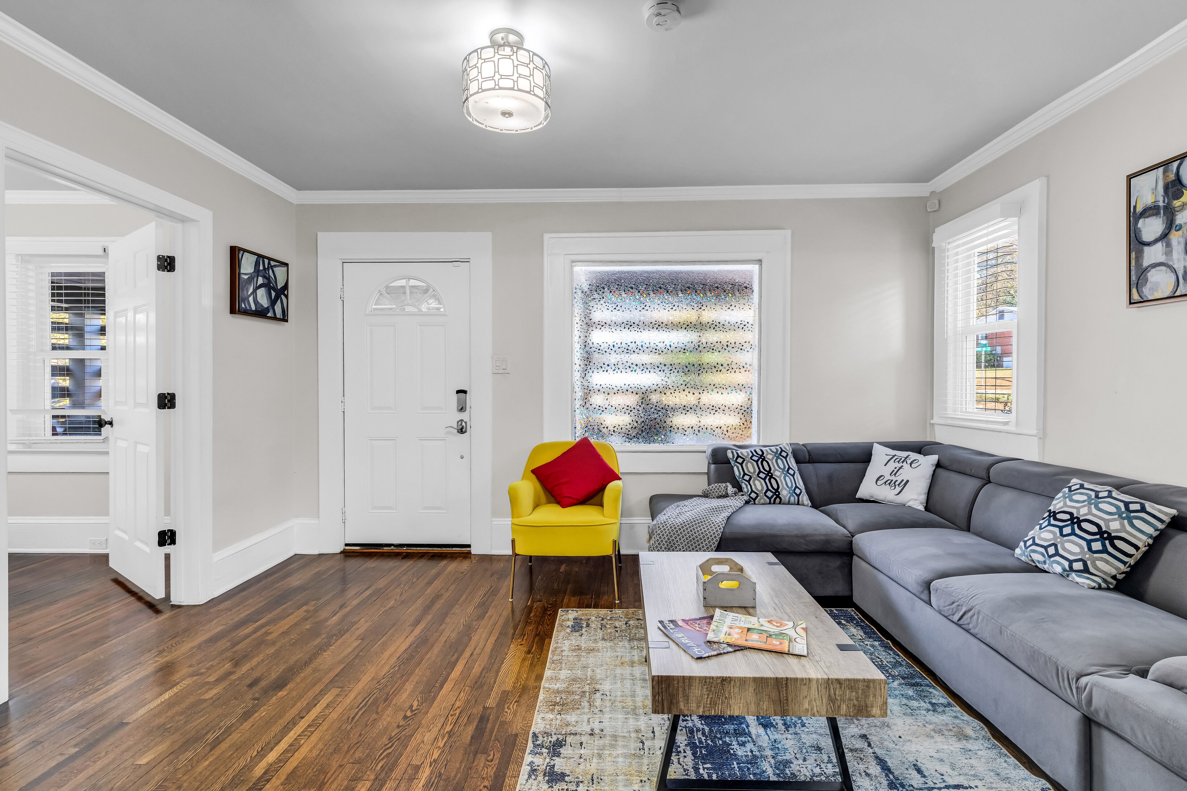 A living room with hardwood flooring, a grey sectional sofa, a yellow armchair, and a coffee table with magazines.