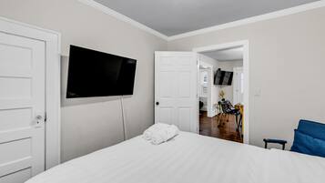 A hotel room with a bed, a TV mounted on the wall, and an open door leading to a dining area.