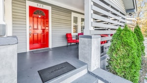 Una puerta roja con el número 820, un porche cubierto con una silla roja y un pequeño arbusto verde.