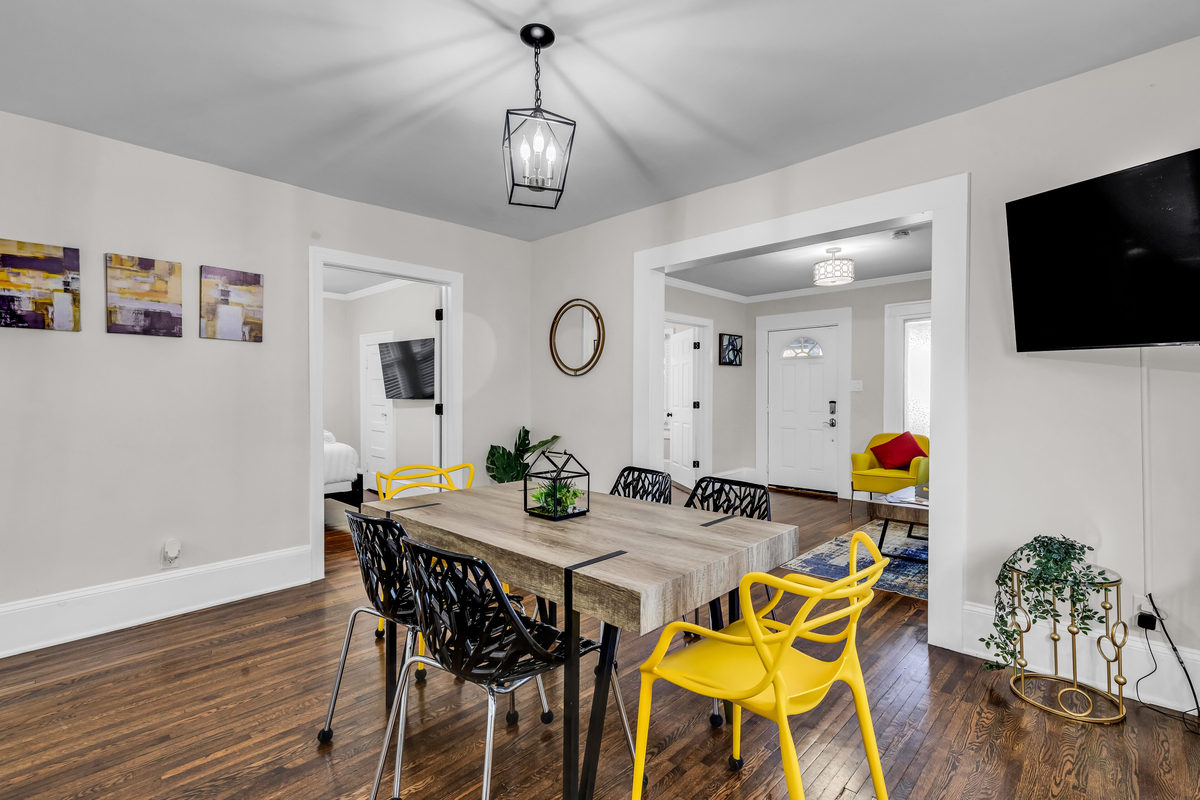 A modern dining area with a wooden table, black and yellow chairs, and a chandelier.