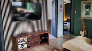 Ein modernes Wohnzimmer mit Flachbildfernseher an einer Wand mit vertikalen Lamellen, einer Holz-Unterhaltungsanlage mit Büchern, einem beigefarbenen Sofa und einem Couchtisch mit Dekoration.