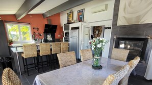 Eine moderne Küche mit Backofen, ein Essbereich mit Korbstühlen und einem Tisch sowie ein Kamin.