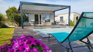 Ein Poolbereich mit überdachter Terrasse, Liegestühlen und Blumenbeeten.