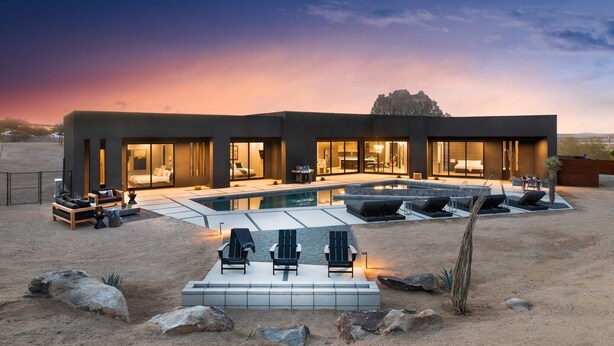 Een modern huis met zwembad, terras en een woestijnlandschap.