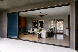 Un salon moderne avec un canapé, une table basse et des plantes. Il y a une grande fenêtre et une porte qui donne sur une autre pièce.