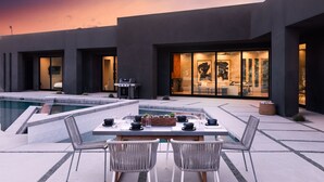 Een moderne, overdekte patio met een zwembad, een barbecue en een eethoek met twee stoelen en een tafel.