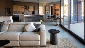 Een moderne woonkamer met een beige hoekbank, een salontafel en een eethoek met een bar.