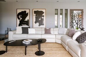 Un salon moderne avec un canapé en cuir blanc, une table basse noire et des tableaux abstraits accrochés au mur.