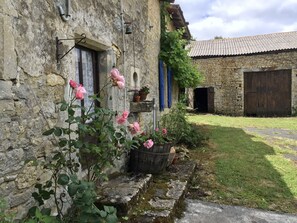 Un edificio in pietra rustica con un'area giardino, tra cui una rosa e piante in vaso.