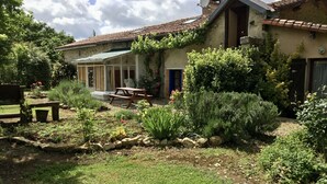 Una casa rústica con jardín, un banco de madera y un patio.