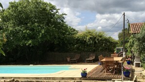 Un patio trasero con piscina, terraza de madera y mobiliario exterior.