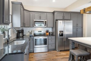 A modern kitchen with grey cabinetry, stainless steel appliances, a built-in oven, and a refrigerator. - Enjoy New Arcades & Outdoor Slide, Private Hot Tub, Close to SDC, Free Tickets & Pickleball (Hollister)