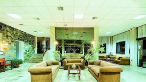 A spacious lobby with a large seating area, a staircase, and a view of a sports field through a glass wall. - Xenios Theoxenia Hotel (Aristotelis)