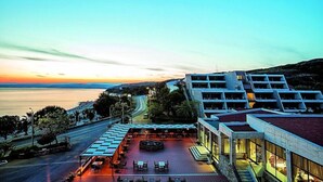 A hotel with a rooftop terrace overlooking a coastal area, featuring outdoor seating and a view of the sea. - Xenios Theoxenia Hotel (Aristotelis)