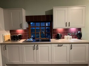 A kitchen with white cabinets, a double sink, and a window with a view of the outside. - Apartment One, The Carriage House. (York)