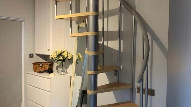 Una escalera espiral moderna con un diseño minimalista, acabado en madera y barandillas de metal.