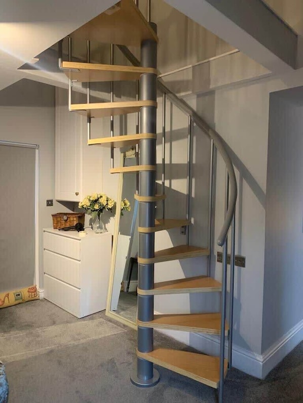 Una escalera espiral moderna con barandillas de metal y peldaños de madera, que conduce a un piso superior.