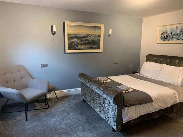 A bedroom with a bed, a chair, and two wall-mounted light fixtures. - Apartment One, The Carriage House. (York)
