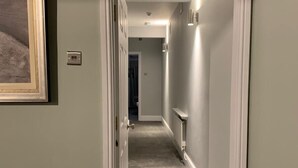 Un pasillo con piso alfombrado, paredes blancas y un cuadro enmarcado a la izquierda.