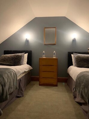 A small, dimly lit room with two beds, a wooden dresser, and two wall-mounted lights. - Apartment One, The Carriage House. (York)