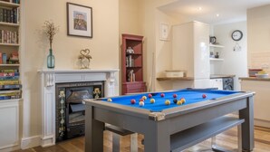 Une table de billard dans une pièce dotée d’une cheminée, de bibliothèques et d’un coin cuisine.