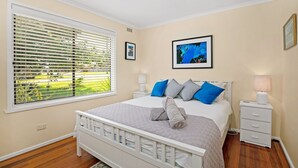 Een slaapkamer met een bed, twee nachtkastjes, een raam met zonwering en twee ingelijste foto’s aan de muur.