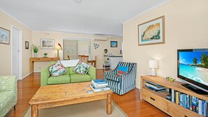 Een gezellige woonkamer met een groene bank, een gestreepte fauteuil, een houten salontafel en een tv-meubel met boeken.