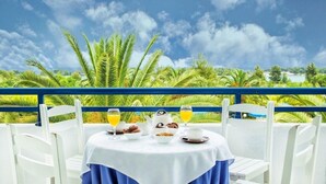 A table set with breakfast items and drinks, overlooking a tropical landscape with palm trees and a clear sky. - Xenios Port Marina (Kassandra)