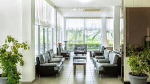A spacious living area with a sofa set, a coffee table, and large windows offering a view of greenery. - Xenios Port Marina (Kassandra)