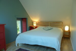 Une chambre à coucher avec un grand lit, une table de chevet avec une lampe, une commode et une fenêtre avec des volets.