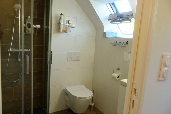 Une salle de bain équipée d’une douche, de toilettes et d’une étagère où sont rangés les articles de toilette.