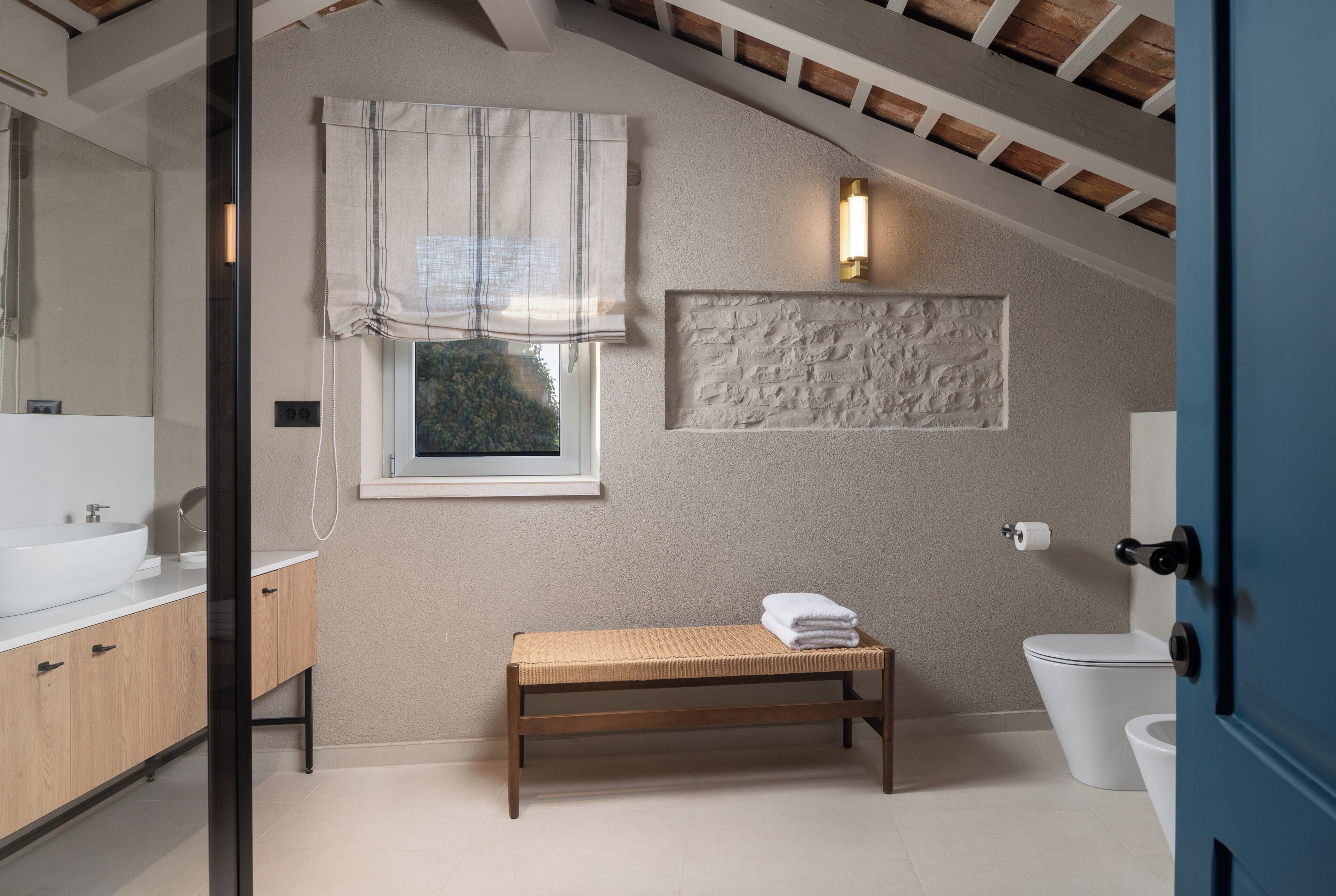 A bathroom with a wooden bench, a large mirror, a white sink, and a toilet.
